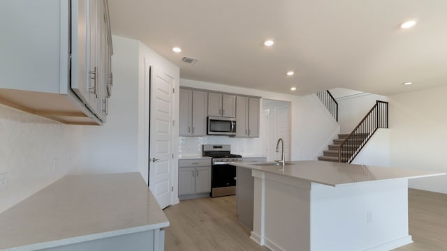 kitchen with decorative backsplash, an island with sink, light hardwood / wood-style flooring, sink, and stainless steel appliances