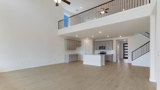 unfurnished living room with sink, light wood-type flooring, a towering ceiling, and ceiling fan