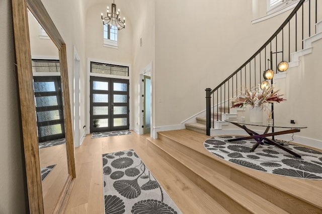 entrance foyer with french doors, a chandelier, a high ceiling, and light wood-type flooring