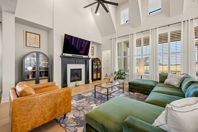 living room featuring a tiled fireplace, high vaulted ceiling, wood-type flooring, and ceiling fan