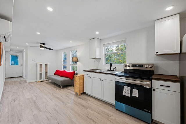 kitchen featuring stainless steel electric range oven, light wood finished floors, dark countertops, white cabinetry, and a sink