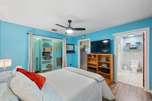 bedroom featuring tile walls, visible vents, ensuite bathroom, ceiling fan, and wood finished floors