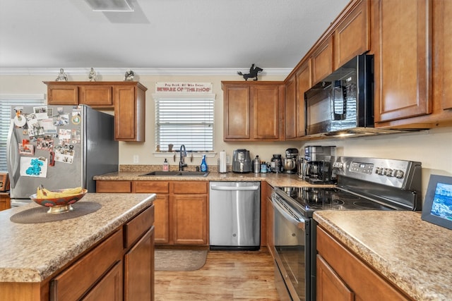 kitchen with crown molding, appliances with stainless steel finishes, sink, and light wood-type flooring