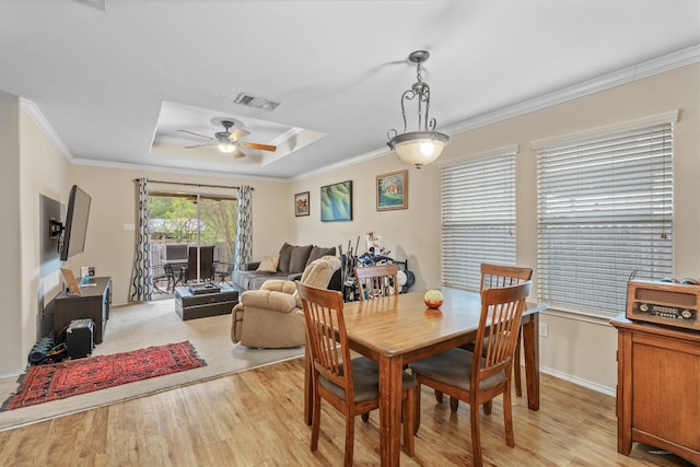 dining space featuring a raised ceiling, ornamental molding, light wood-type flooring, and ceiling fan