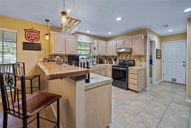 kitchen with light brown cabinetry, kitchen peninsula, decorative light fixtures, black / electric stove, and decorative backsplash