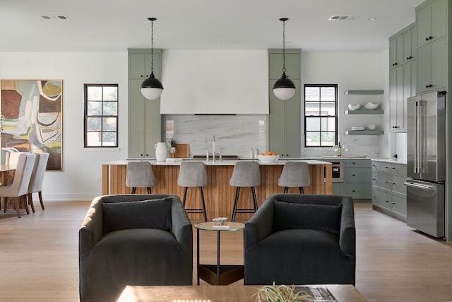 kitchen featuring high end fridge, decorative light fixtures, backsplash, and light hardwood / wood-style floors