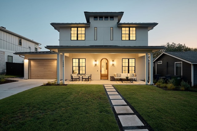 back house at dusk with a patio, outdoor lounge area, and a lawn