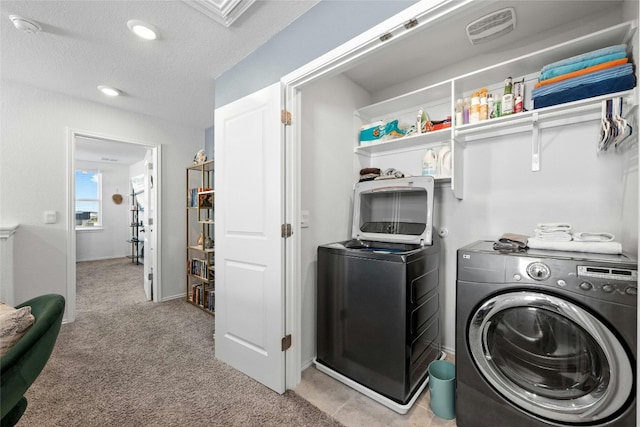 clothes washing area with light carpet, a textured ceiling, and washing machine and clothes dryer