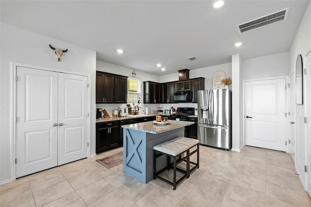 kitchen with light stone countertops, a kitchen bar, black appliances, dark brown cabinetry, and a center island