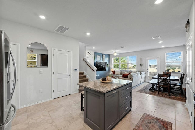 kitchen featuring light stone countertops, a center island, ceiling fan, stainless steel refrigerator, and light tile patterned floors