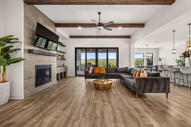 living room featuring ceiling fan, beamed ceiling, light wood-type flooring, and a fireplace