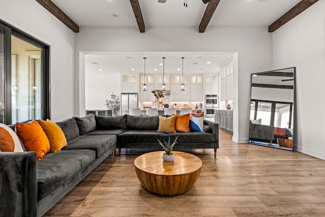 living room with ceiling fan, beamed ceiling, and light hardwood / wood-style flooring