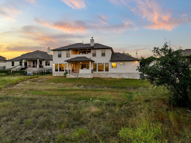 back house at dusk featuring a lawn