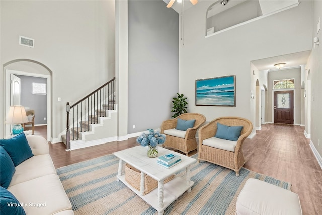 living room with ceiling fan, a towering ceiling, and hardwood / wood-style floors