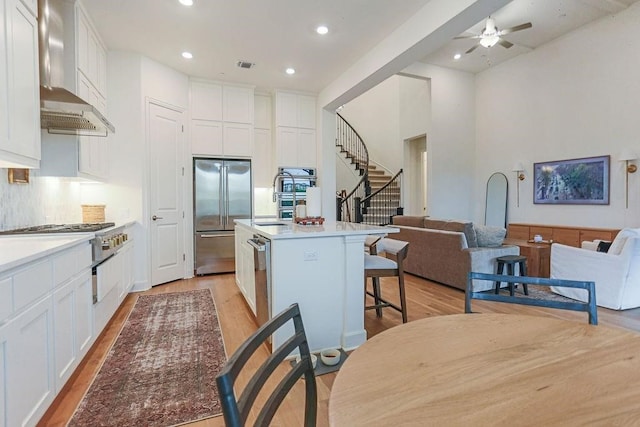 kitchen with wall chimney exhaust hood, a center island, appliances with stainless steel finishes, and white cabinetry