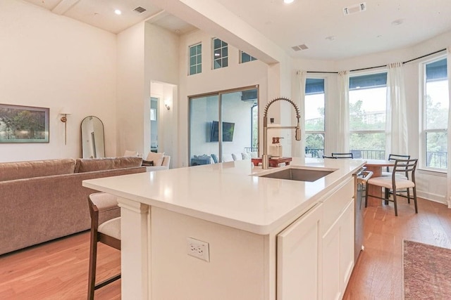 kitchen with a center island with sink, a breakfast bar, white cabinetry, light wood-type flooring, and sink