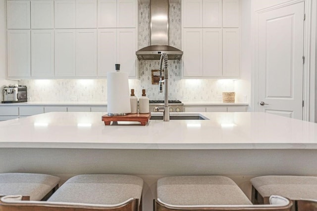 kitchen featuring wall chimney range hood, a kitchen island with sink, and a kitchen bar