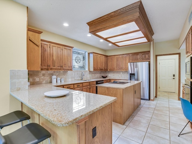 kitchen with light tile patterned floors, sink, a kitchen breakfast bar, black appliances, and a kitchen island