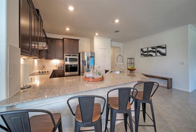 kitchen with dark brown cabinetry, stainless steel appliances, crown molding, and a sink