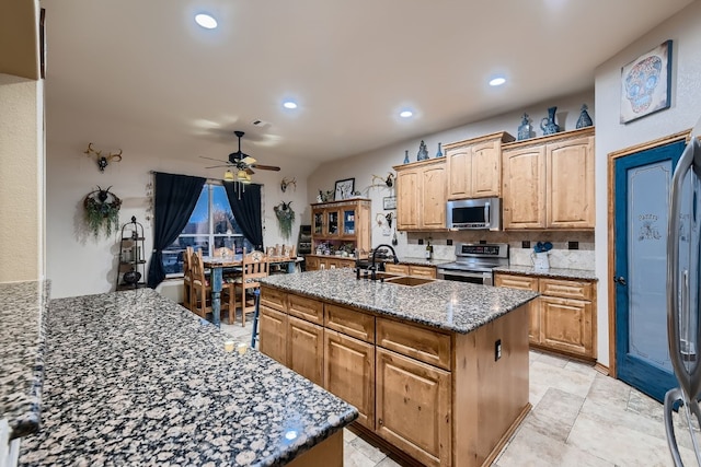 kitchen featuring appliances with stainless steel finishes, dark stone countertops, sink, and a center island with sink