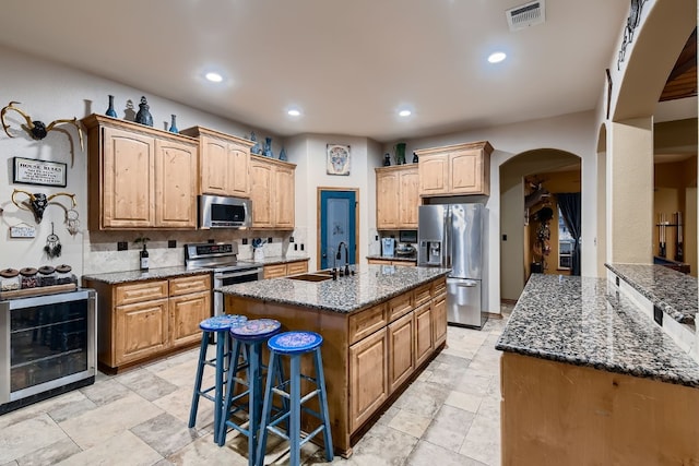 kitchen with a breakfast bar area, an island with sink, stainless steel appliances, sink, and beverage cooler