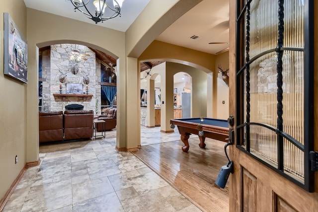 rec room with pool table, light wood-type flooring, ceiling fan with notable chandelier, and a stone fireplace