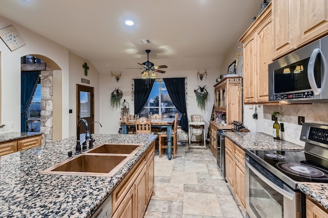 kitchen featuring stone counters, light brown cabinetry, appliances with stainless steel finishes, sink, and ceiling fan