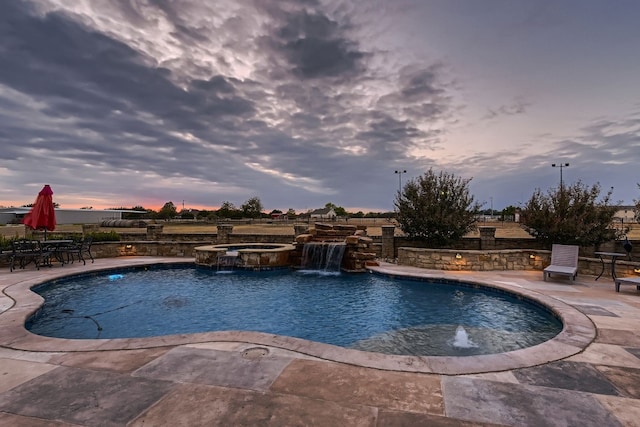 pool at dusk featuring a patio area, pool water feature, and an in ground hot tub