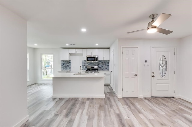 kitchen with decorative backsplash, an island with sink, stainless steel appliances, white cabinets, and light hardwood / wood-style floors