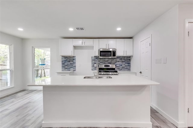 kitchen with appliances with stainless steel finishes, white cabinets, and an island with sink