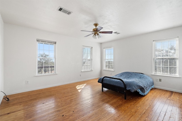 bedroom with ceiling fan, a textured ceiling, multiple windows, and light hardwood / wood-style floors