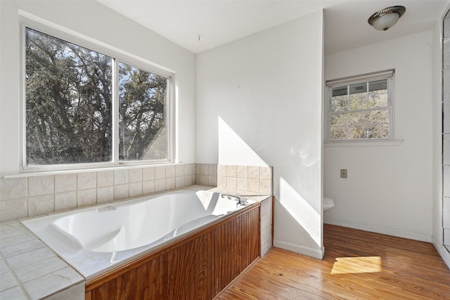 bathroom with a healthy amount of sunlight, toilet, wood-type flooring, and a tub to relax in