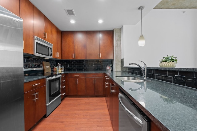 kitchen with decorative light fixtures, sink, dark stone countertops, stainless steel appliances, and light hardwood / wood-style flooring