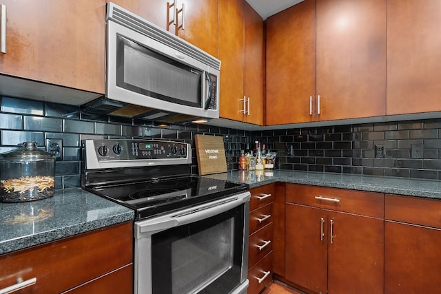 kitchen with stainless steel appliances, brown cabinetry, dark stone countertops, and backsplash