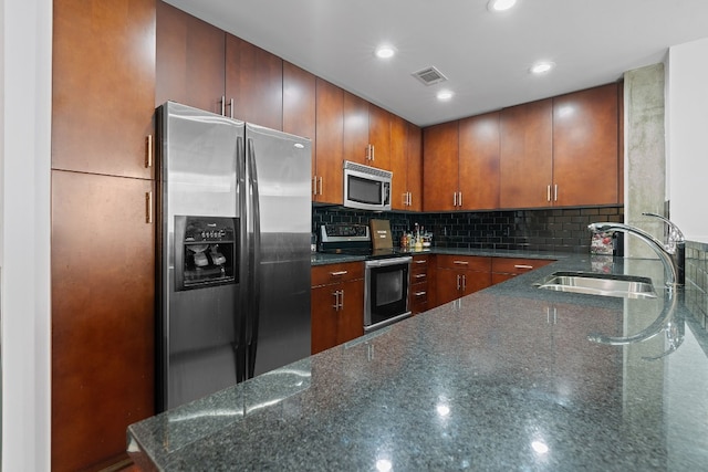 kitchen with sink, tasteful backsplash, dark stone counters, kitchen peninsula, and stainless steel appliances