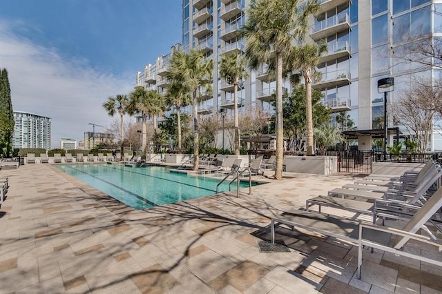 community pool with a view of city, a patio, and fence