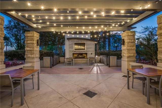 patio terrace at dusk featuring an outdoor stone fireplace, visible vents, and fence