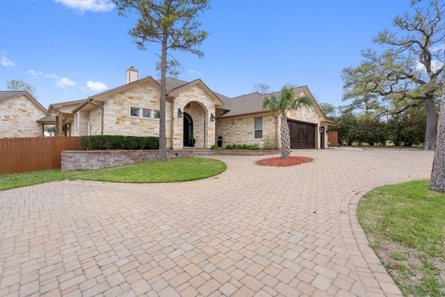 111 Kolekole Ln, Bastrop, TX 78602 - french country home featuring stone siding, an attached garage, curved driveway, and a chimney
