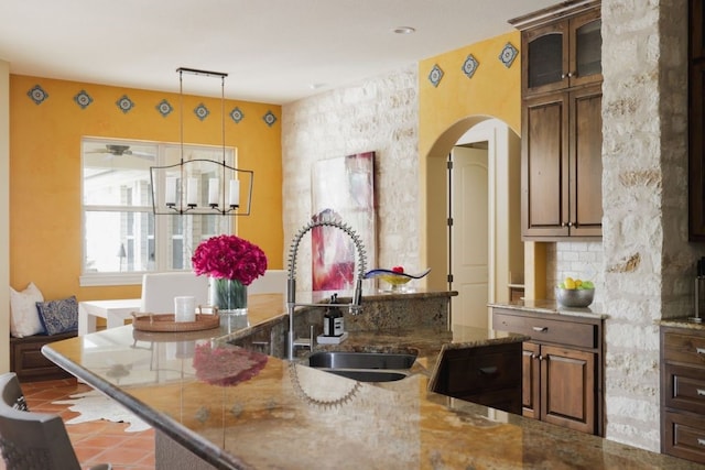 kitchen with tile patterned floors, dark stone counters, sink, pendant lighting, and a chandelier