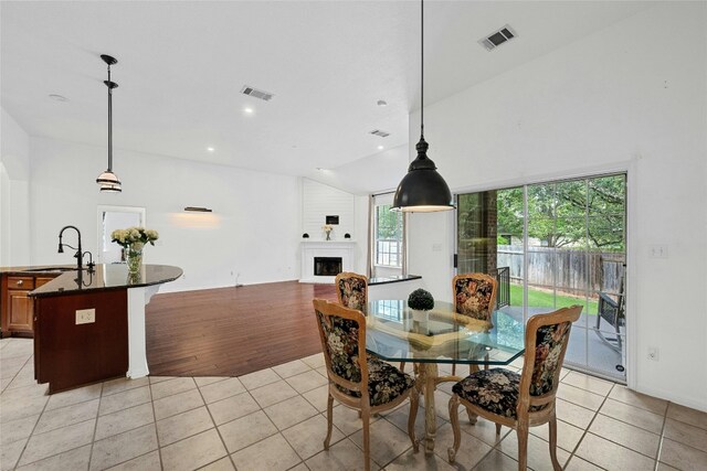 dining room featuring sink, a large fireplace, vaulted ceiling, and light hardwood / wood-style flooring