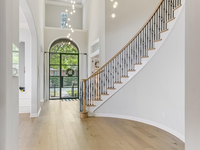 entryway with ornamental molding, a notable chandelier, hardwood / wood-style flooring, and a towering ceiling