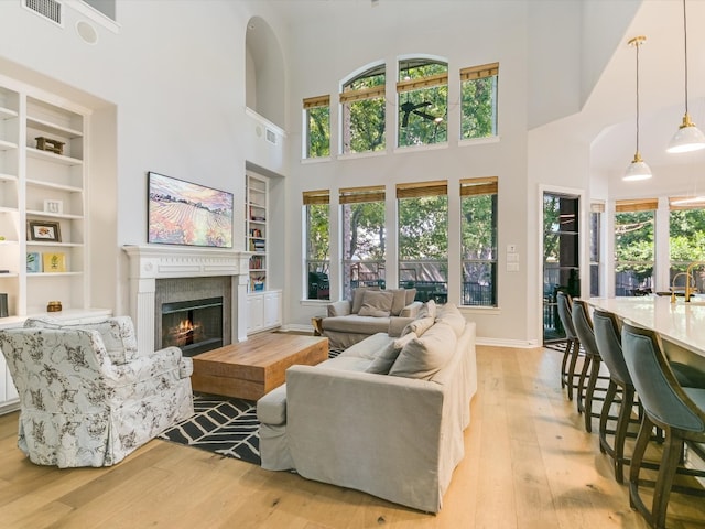 living room featuring a towering ceiling, built in features, and light wood-type flooring