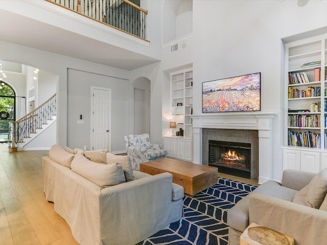 living room with a towering ceiling, built in features, and light wood-type flooring