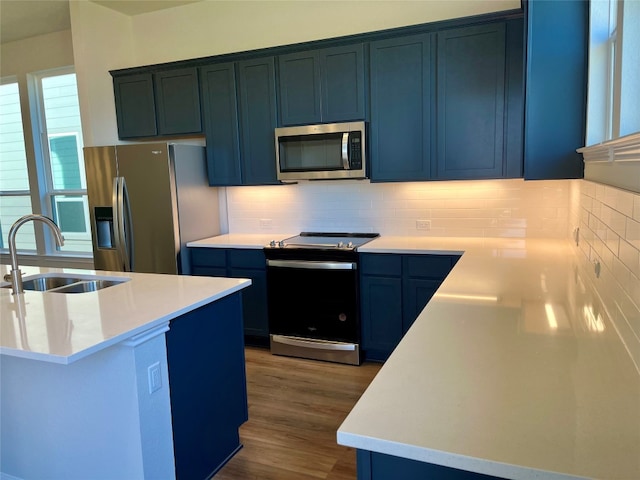 kitchen featuring dark wood-type flooring, sink, blue cabinetry, appliances with stainless steel finishes, and tasteful backsplash