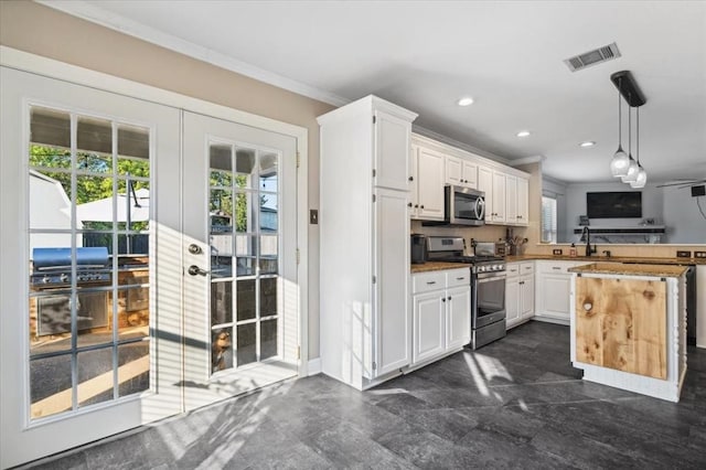 kitchen with kitchen peninsula, crown molding, white cabinets, decorative light fixtures, and appliances with stainless steel finishes