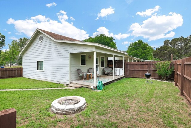 back of house with an outdoor fire pit, a wooden deck, and a lawn