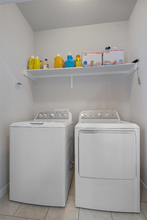 laundry area with a textured ceiling, washing machine and clothes dryer, and light tile patterned floors