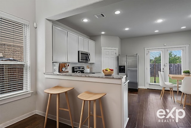 16304 Travesia Way, Austin, TX 78728 - kitchen with stainless steel appliances, a peninsula, decorative backsplash, dark wood-style flooring, and light stone countertops