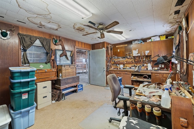 office space featuring a workshop area, light colored carpet, ceiling fan, and wood walls