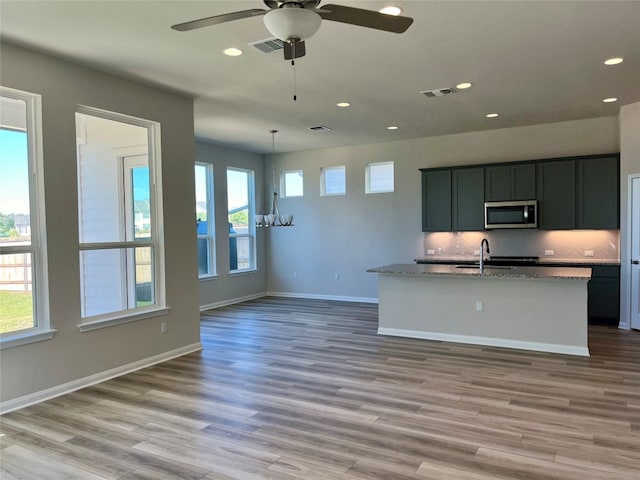 kitchen with decorative backsplash, light stone counters, sink, wood-type flooring, and hanging light fixtures